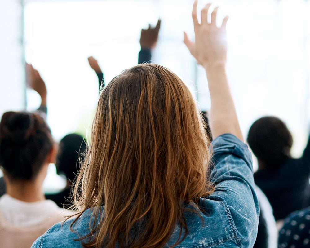 Rearview shot of a group of businesspeople raising their hands to ask questions during a conference